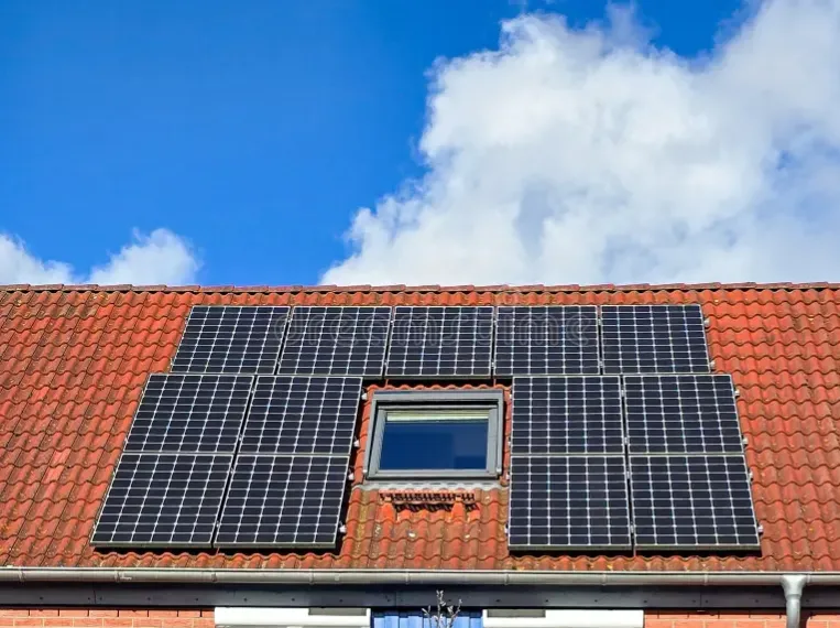 Painéis solares num telhado de telha, à volta de uma janela