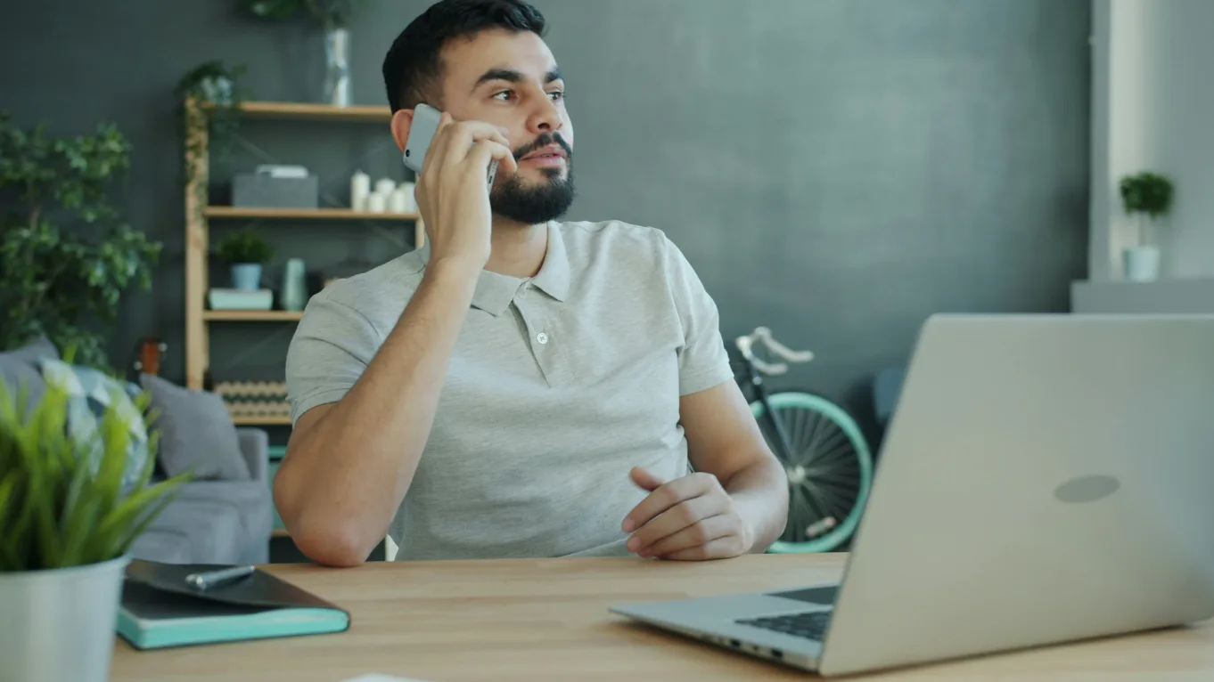 Homem ao telefone, sentado a uma secretária com um portátil